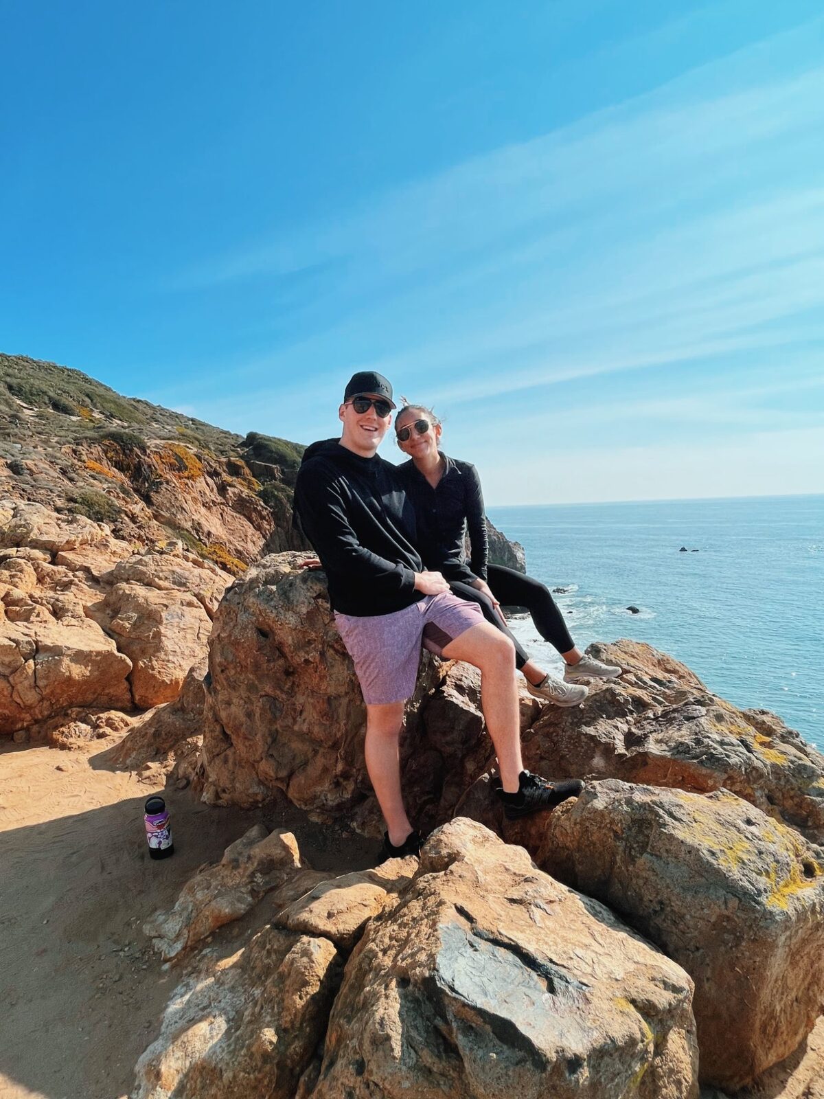 The couple sitting on sunlit rocks above the ocean