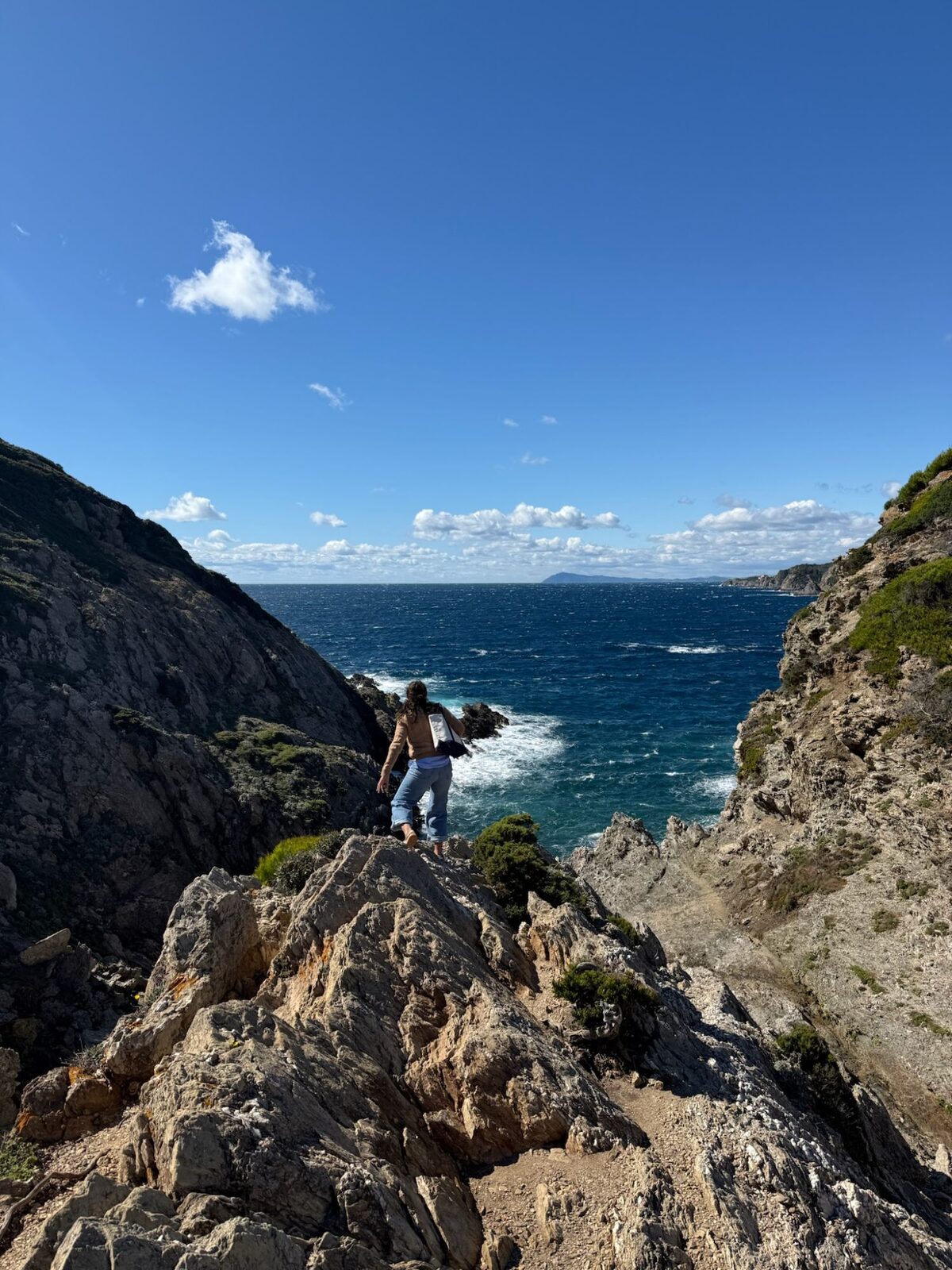 Maddie climbing over rocks toward a bright blue cove