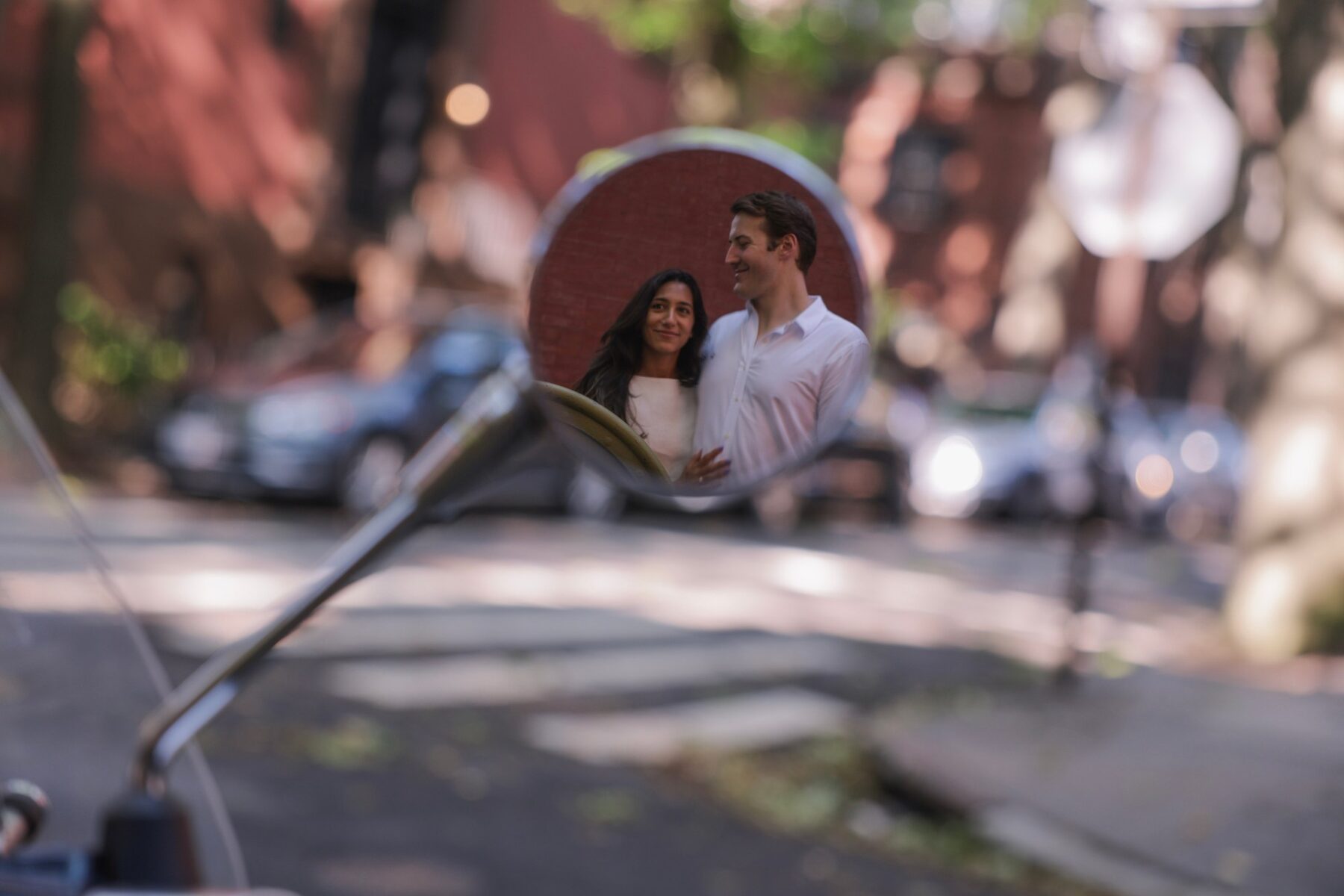 The couple reflected in the round mirror of a scooter on a brick-lined street