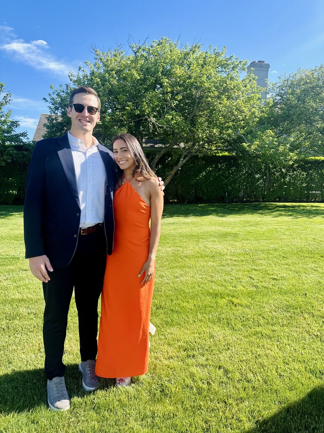 Ryan in a navy blazer and Maddie in an orange dress on a sunny green lawn