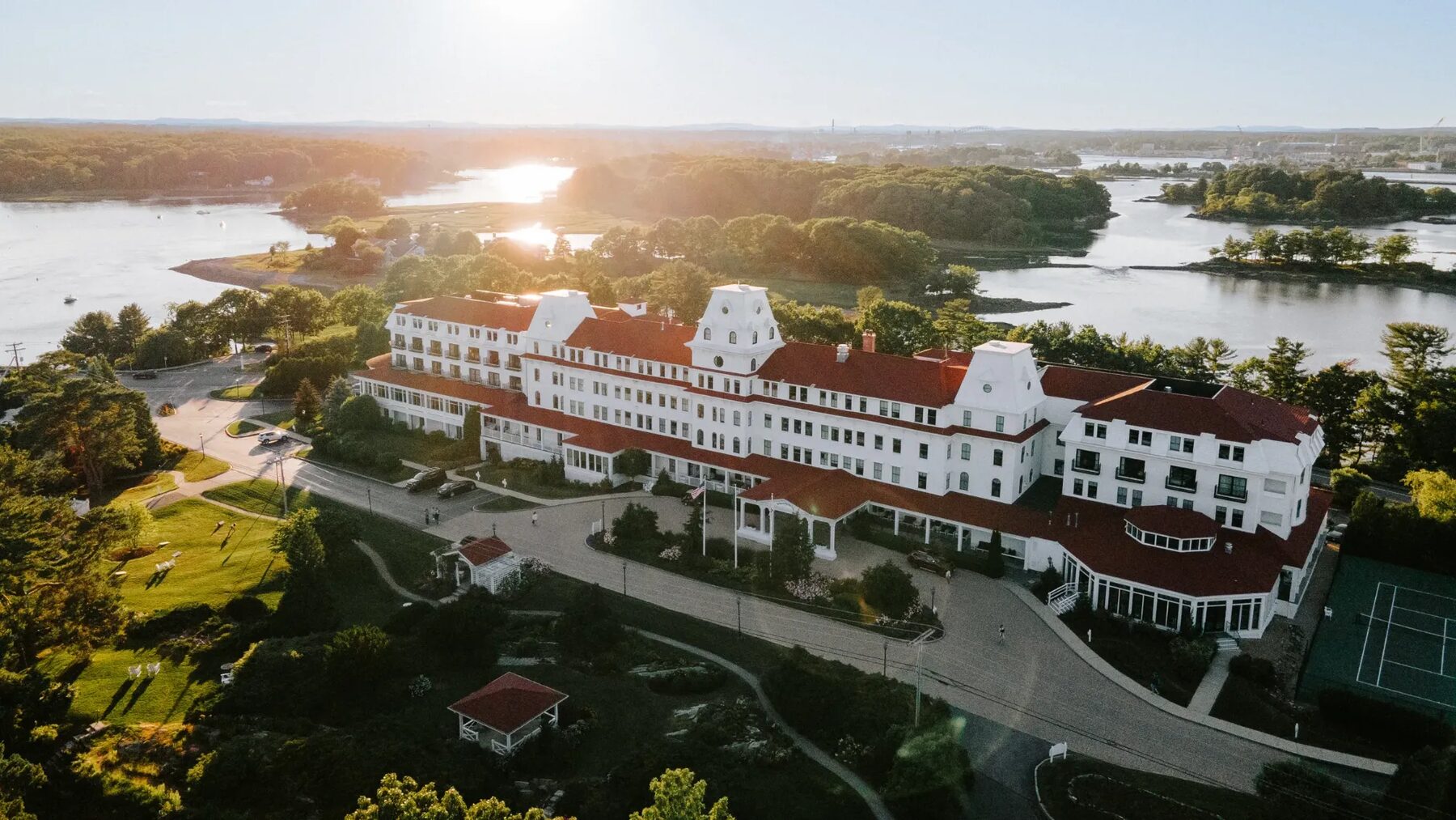Aerial view of the white, red-roofed Wentworth by the Sea hotel surrounded by water at sunset