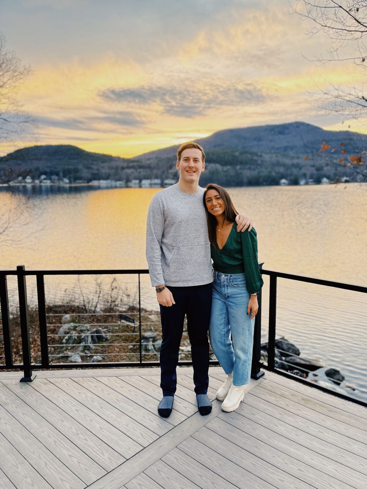 The couple on a deck above a lake at sunset, mountains behind