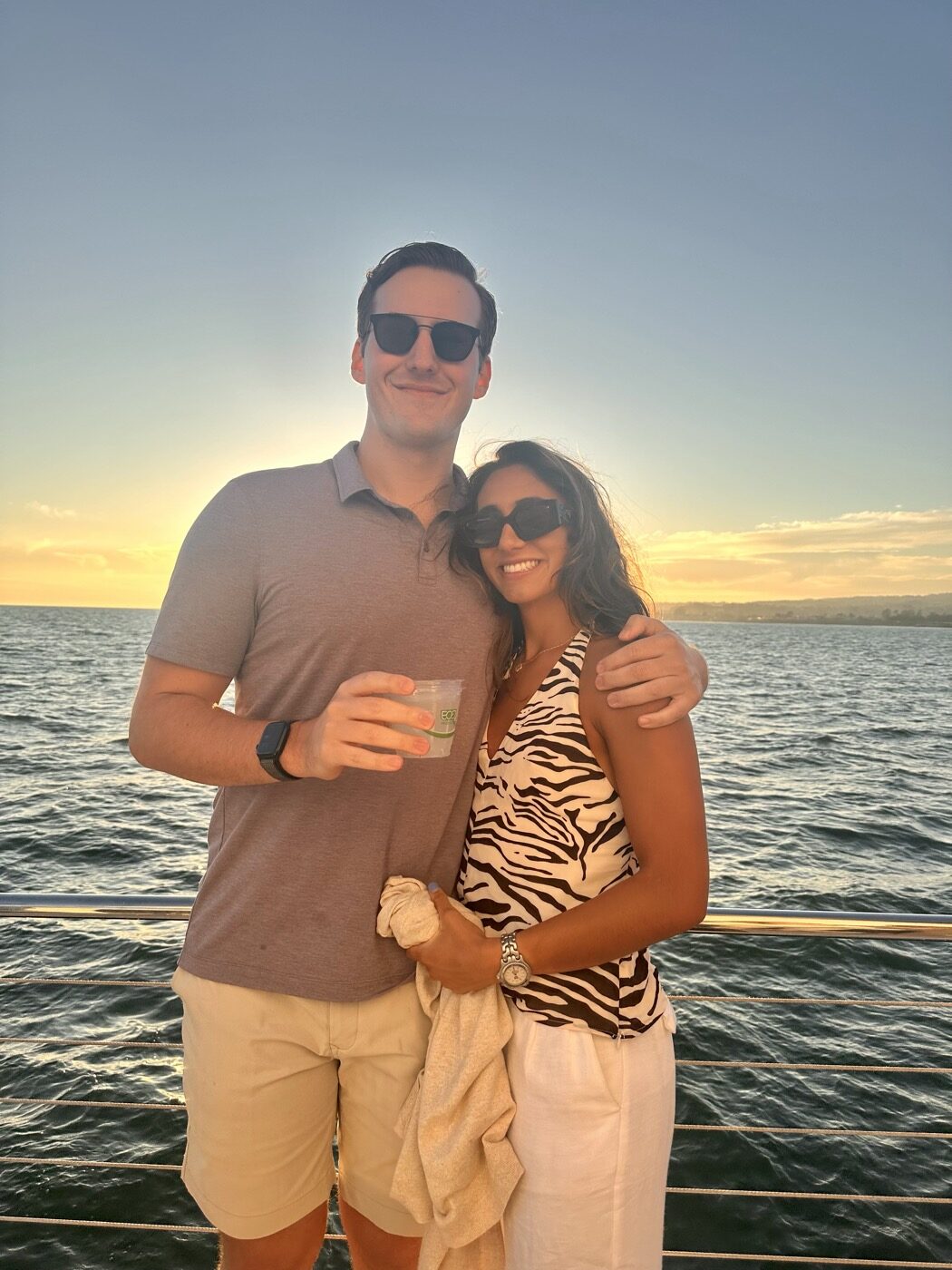 The couple at the rail of a boat at sunset, the sea glowing behind them